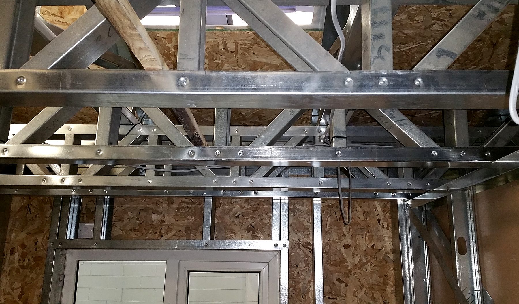 Galvanised light gauge steel roof trusses above a steel stud wall with window opening, before lining
