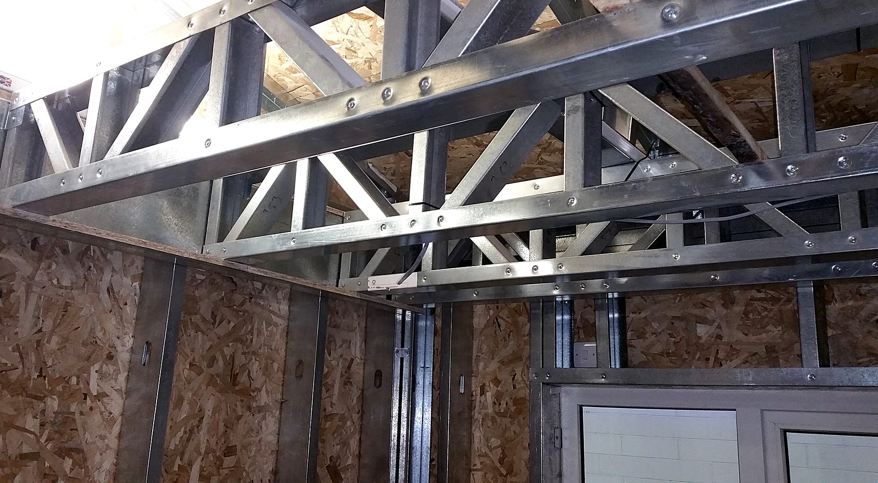 Light gauge steel lattice trusses meeting a stud wall corner with OSB sheathing
